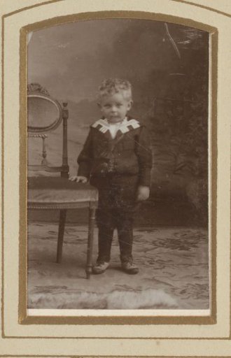 Portrait of a boy, standing by a chair