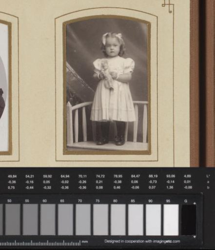Portrait of a girl holding a doll, standing on a wooden bench