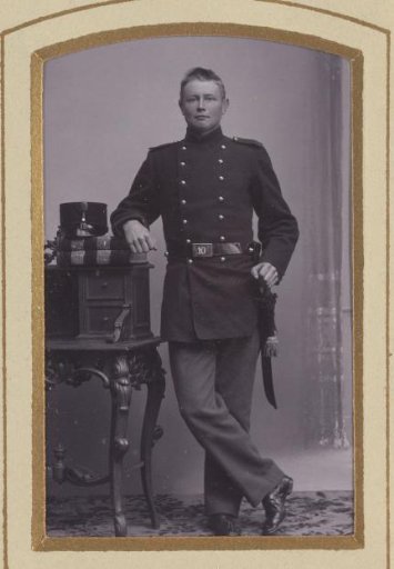 Portrait of a standing young man in uniform, leaning on a writing desk