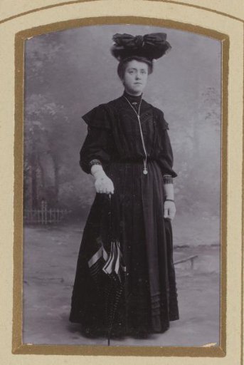 Portrait of a standing woman in a black dress with hat and umbrella, identified as Grietje Knol