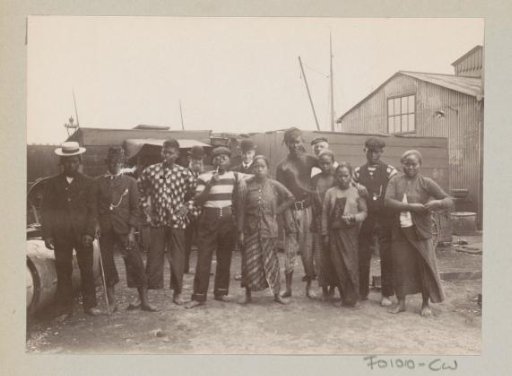 Indonesian men and women, with European men in the background, presumably on a harbour area