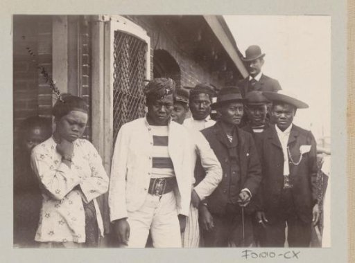 Indonesian men and women, with a European man in the background, presumably on a harbour area