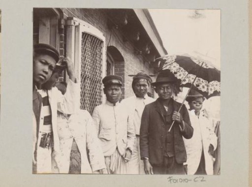 Men and women in front of a small house, presumably on a harbour area