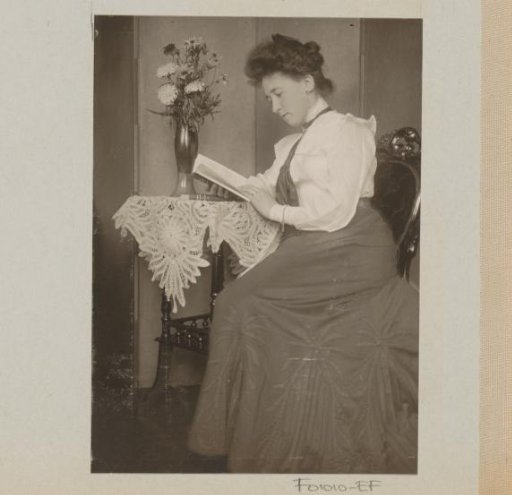 Woman reading a book, seated at a table with a vase of flowers