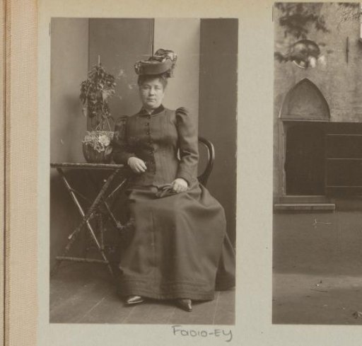 Woman wearing a hat, seated beside a table with a plant