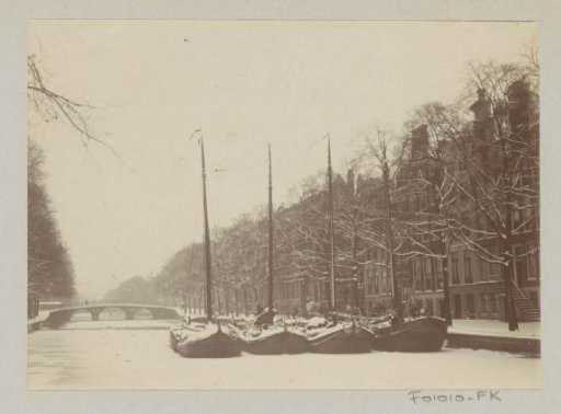 Frozen Amsterdam canal with boats and a bridge