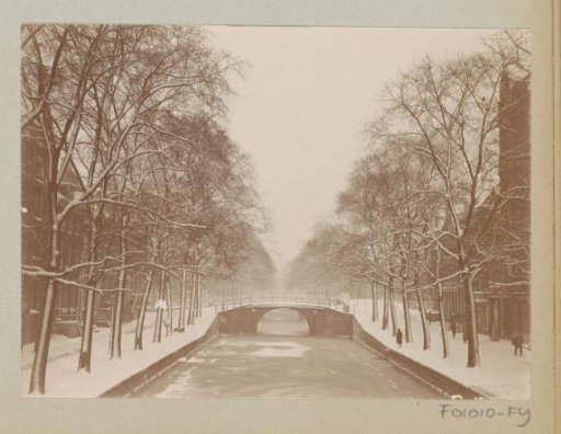 Snow-covered canal with a bridge and trees in Amsterdam