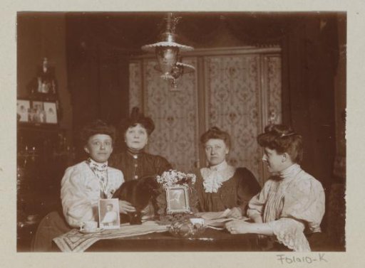 Four women at a table with two photo portraits and a cat on it