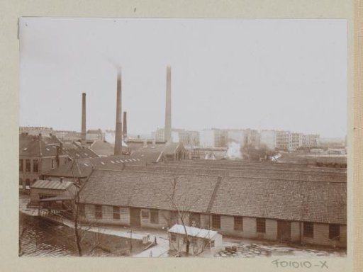 Exterior of factory buildings with chimneys, wooden barrels in the foreground