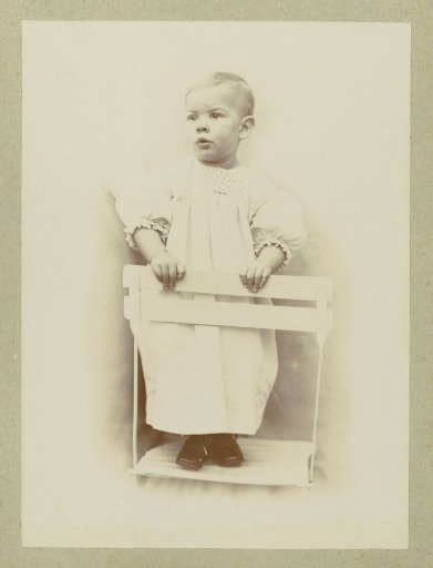 Portrait of a young child in a dress, standing on a chair
