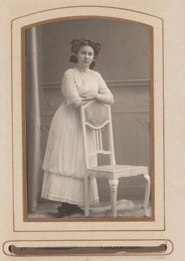Portrait of a woman, standing by a chair
