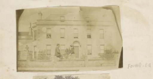 Man and a girl sitting on a fence in front of a country house, probably in Whatley
