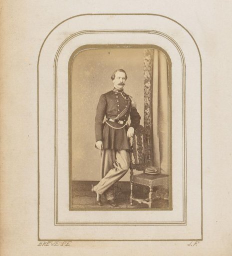 Portrait of a man in uniform, standing by a chair with a hat