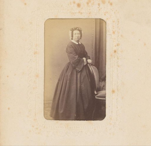 Portrait of a woman with a cap, standing by a chair