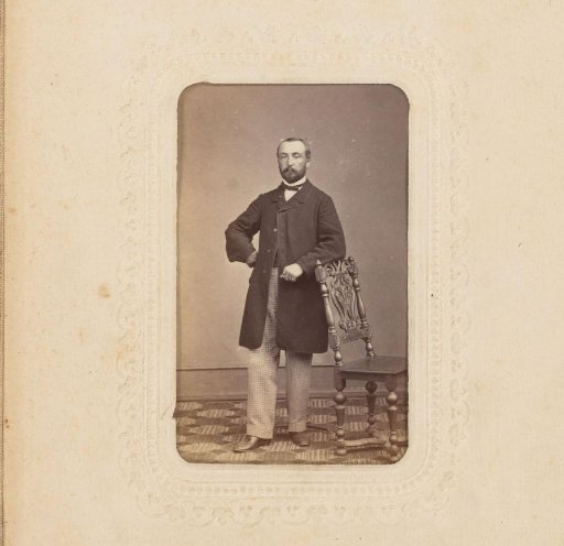 Portrait of a man with a beard, standing by a chair