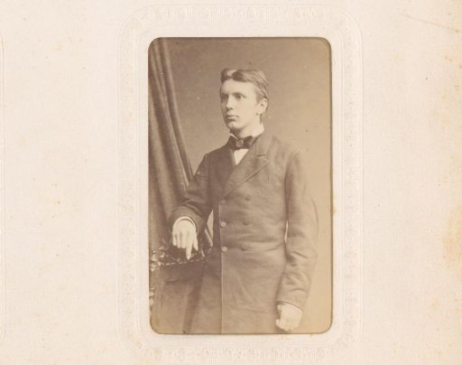 Portrait of a young man with a bow tie, standing by a chair