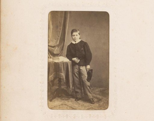 Portrait of a Boy with Cap in Hand, Standing by a Table with Books