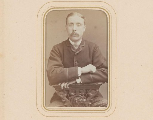 Portrait of a seated man with a moustache, leaning on the arm of a prayer stool