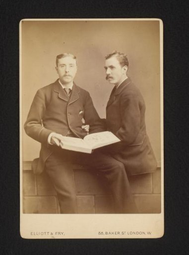 Portrait of two men, seated on a wall, one holding an open book