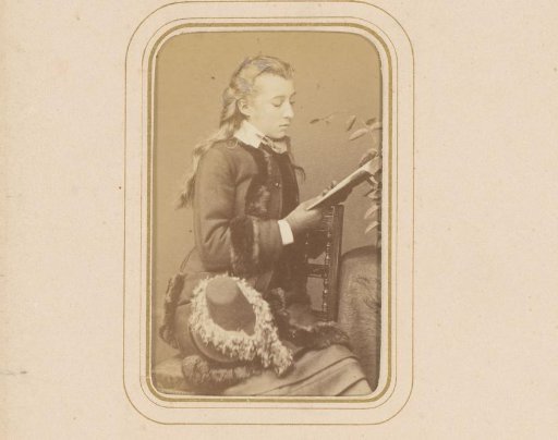 Portrait of a reading girl, seated on a chair with a hat on her lap