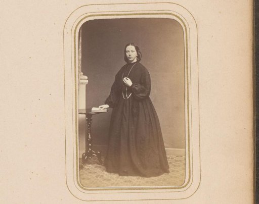 Portrait of a woman, standing by a table with a hand on an open book