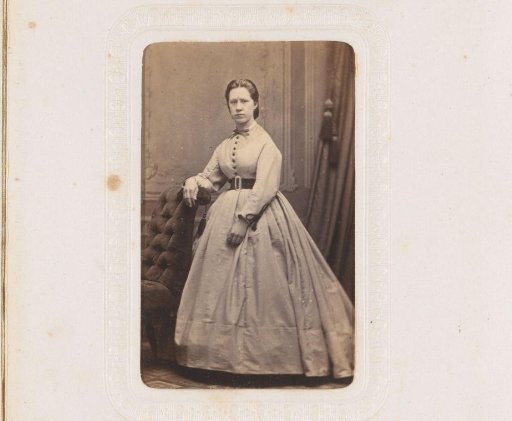 Portrait of a woman, standing by an armchair