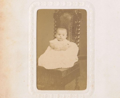 Portrait of a baby in a christening gown, seated on a chair