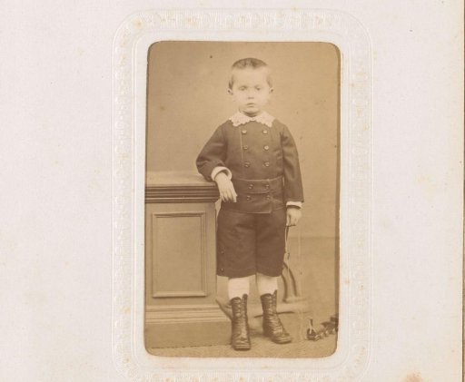Portrait of a boy with a toy train on a string, standing by a pillar