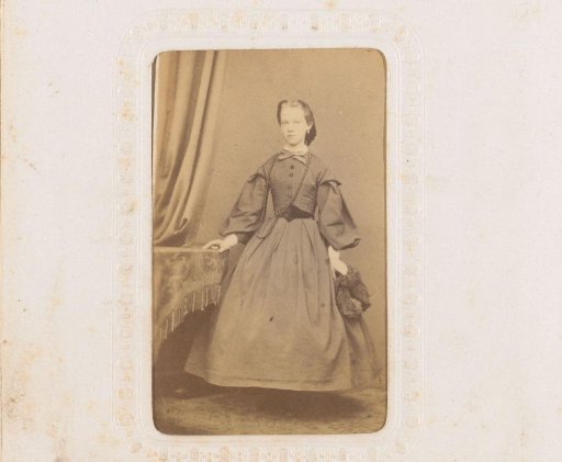 Portrait of a young woman with a hat in her hand, standing by a table