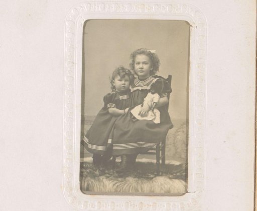 Portrait of two girls, one of whom is sitting on a chair with a doll in her hand