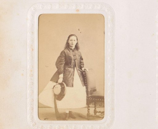 Portrait of a girl with a hat in her hand, standing by a chair
