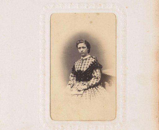 Portrait of a seated young woman in a checkered dress, with an open photo album on her lap