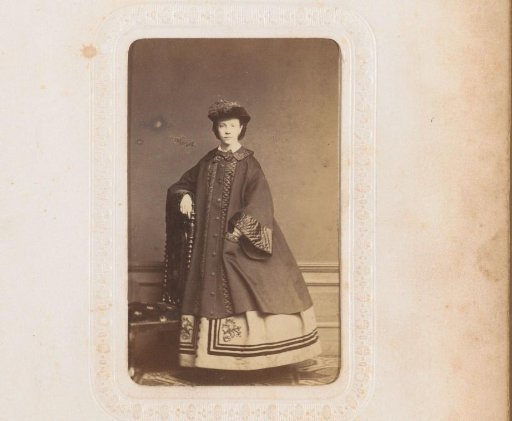 Portrait of a woman with a cloak and hat, standing by a chair