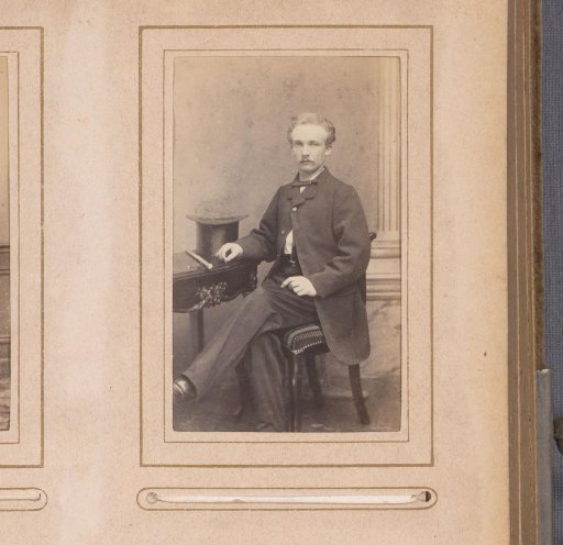 Portrait of a man seated at a table with a tall hat