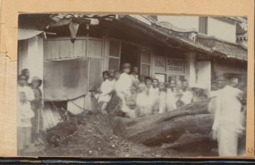 Bystanders around an uprooted tree in front of a barber in Surabaya