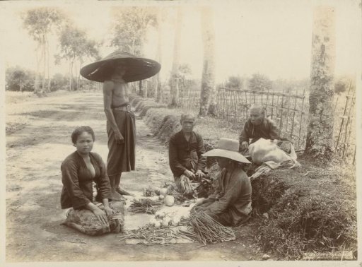 Women and man with vegetables displayed by the roadside