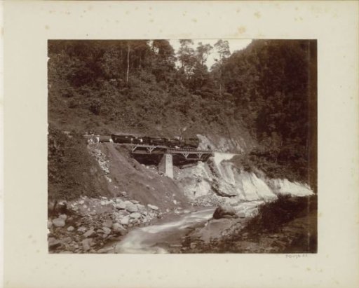 Men posing by a train on a railway bridge over a stream in the Dutch East Indies