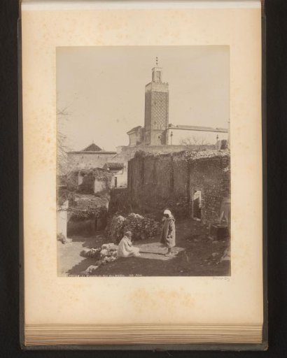Two men on the street with the tower of the Sidi Boumediene Mosque in the background
