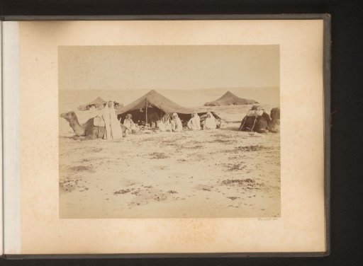 Figures with dromedaries in front of a room in the Sahara