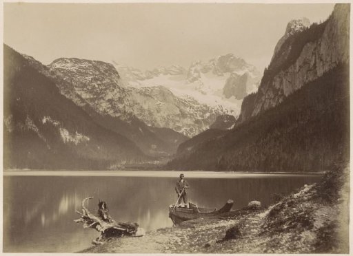 View of a lake and surrounding mountains with a man standing in a boat in the foreground, probably in the Alps