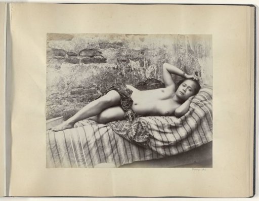 Portrait of a young half-nude Indonesian woman lying on a divan, possibly in Sumatra