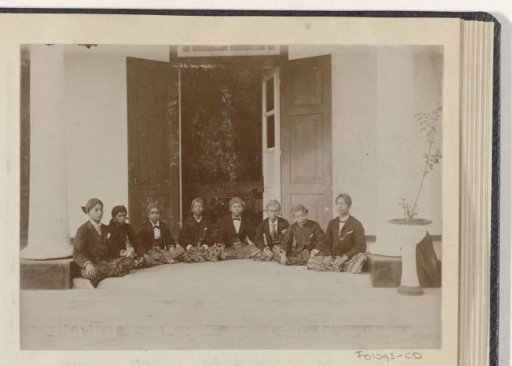 Eight young men seated on the floor at an entrance to a building