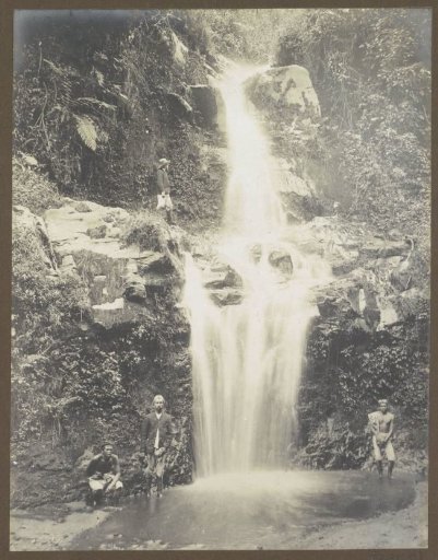 Three Indonesian people and (presumably) a Dutchman at a waterfall in the Dutch East Indies