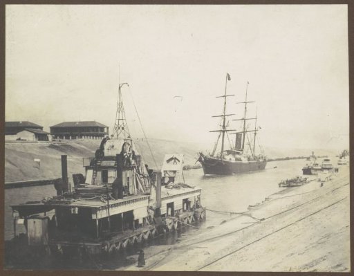 Ship sailing through the Suez Canal near a dredger and houses