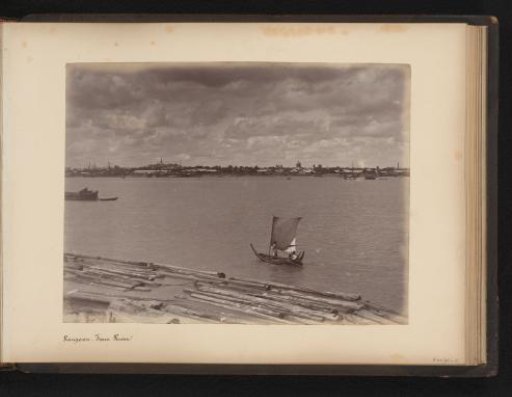 Yangon seen across the river with a sailboat and floating logs in the foreground, Myanmar