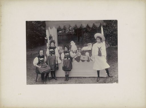 Group portrait of children in costume at a stall with toys, presumably in Sydney
