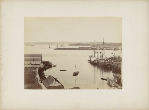 View of a harbour with in the foreground the boat rental and shipbuilding company of B. Macbeth, presumably in Sydney