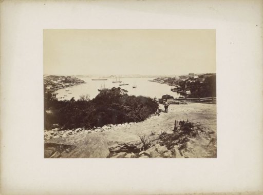 View of the harbour of Sydney with two men on rocky terrain in the foreground