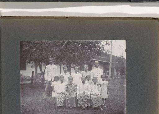 Group portrait of men, women, and children in front of a building, probably on the grounds of a hospital in the Dutch East Indies