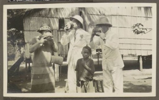 Two men in tropical clothing and a woman drinking from bowls, a boy in the foreground